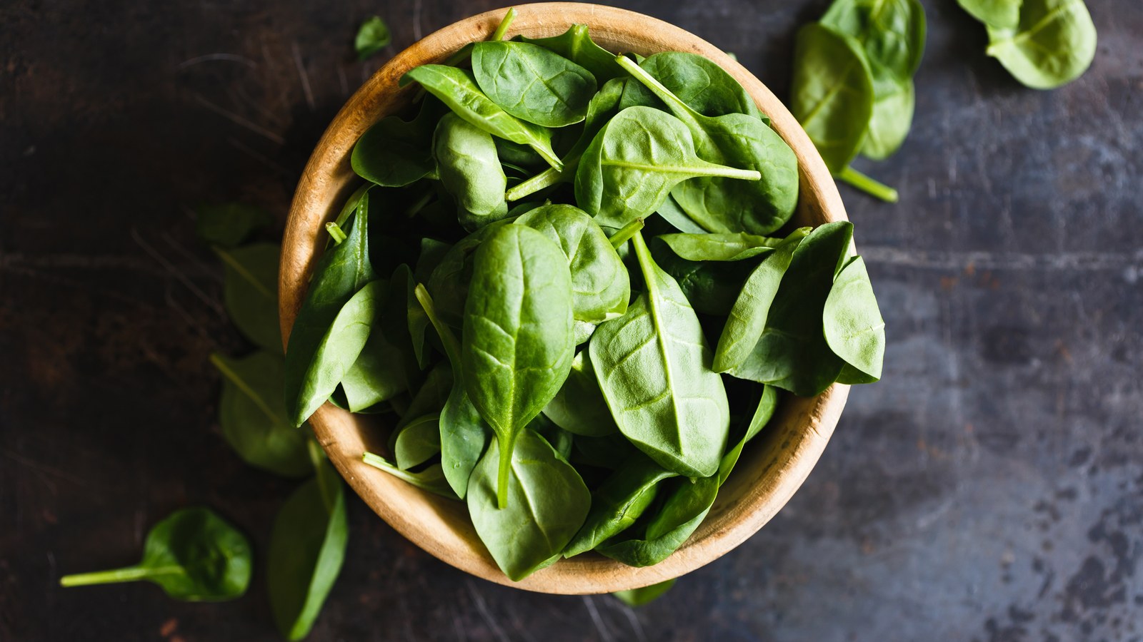 Fresh spinach leaves in a wooden bowl on a dark surface
