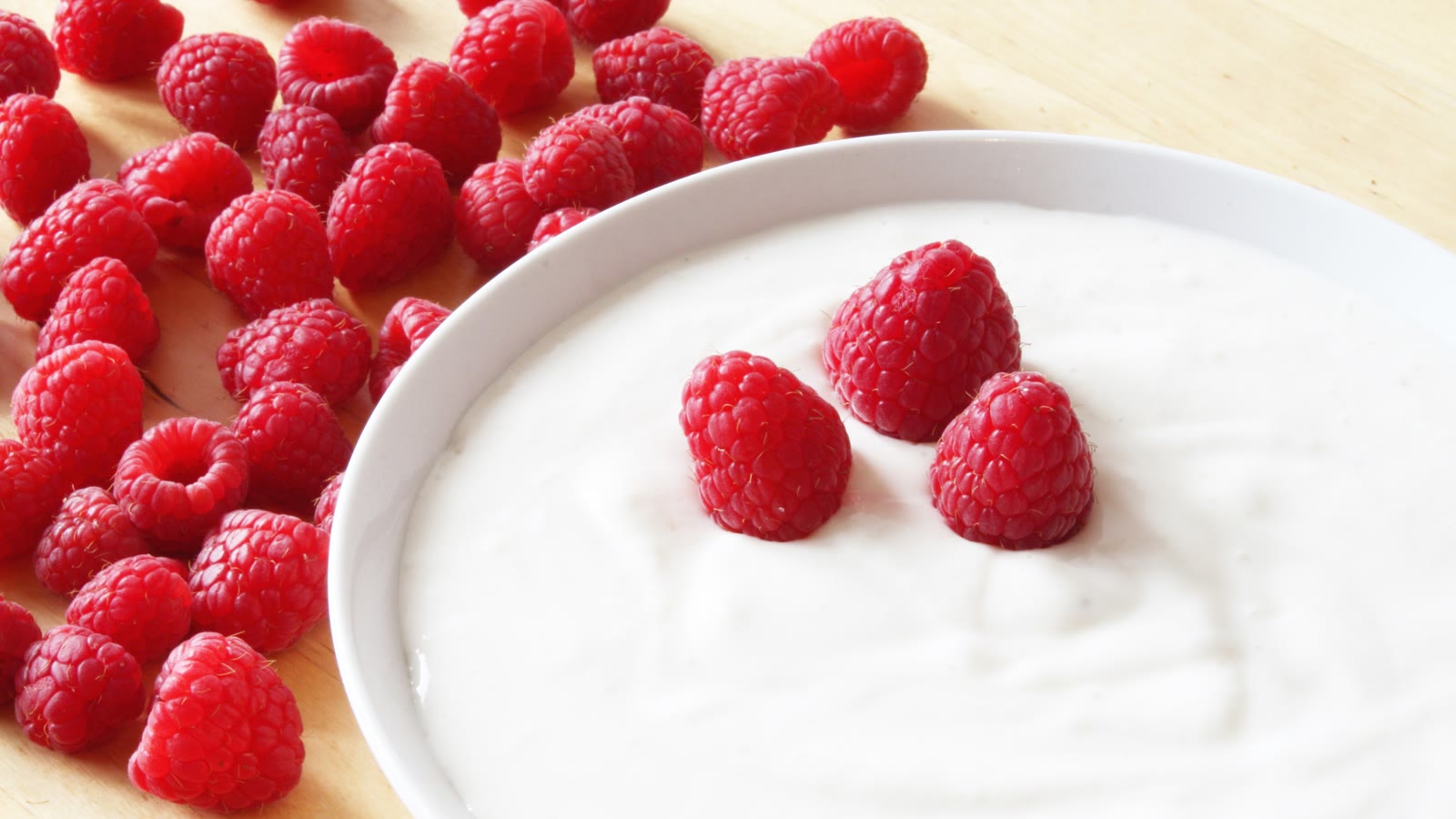 Raspberries piled over yogurt in a white bowl.